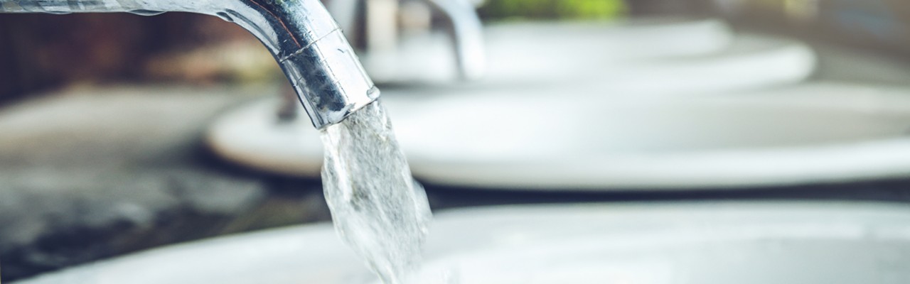 A row of chrome faucets with water droplets on them.