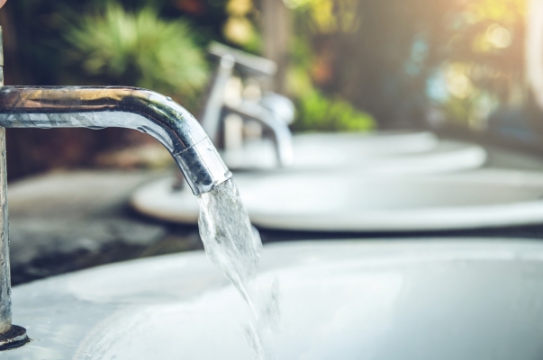 A row of chrome faucets with water droplets on them.